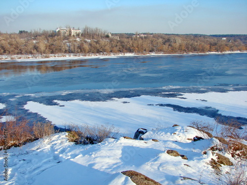 Panorama from the top of the hill of the frozen Dnieper covered with strong ice and dressed in a snow blanket on a frosty sunny day at sunset.