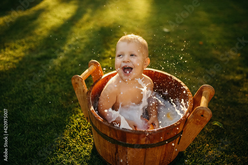 baby splashes in a basin in nature on a green tvava, at sunset. Good mood, child's smile, happiness from swimming in water, water splashes fly, good summer day