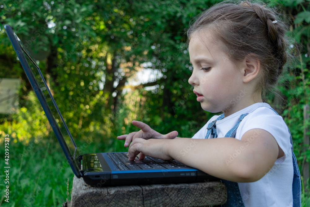 Little girl learning to use laptop in summer in the garden Little girl learning to use laptop in summer in the garden