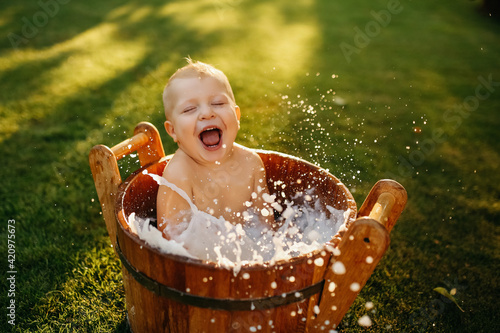 baby splashes in a basin in nature on a green tvava, at sunset. Good mood, child's smile, happiness from swimming in water, water splashes fly, good summer day