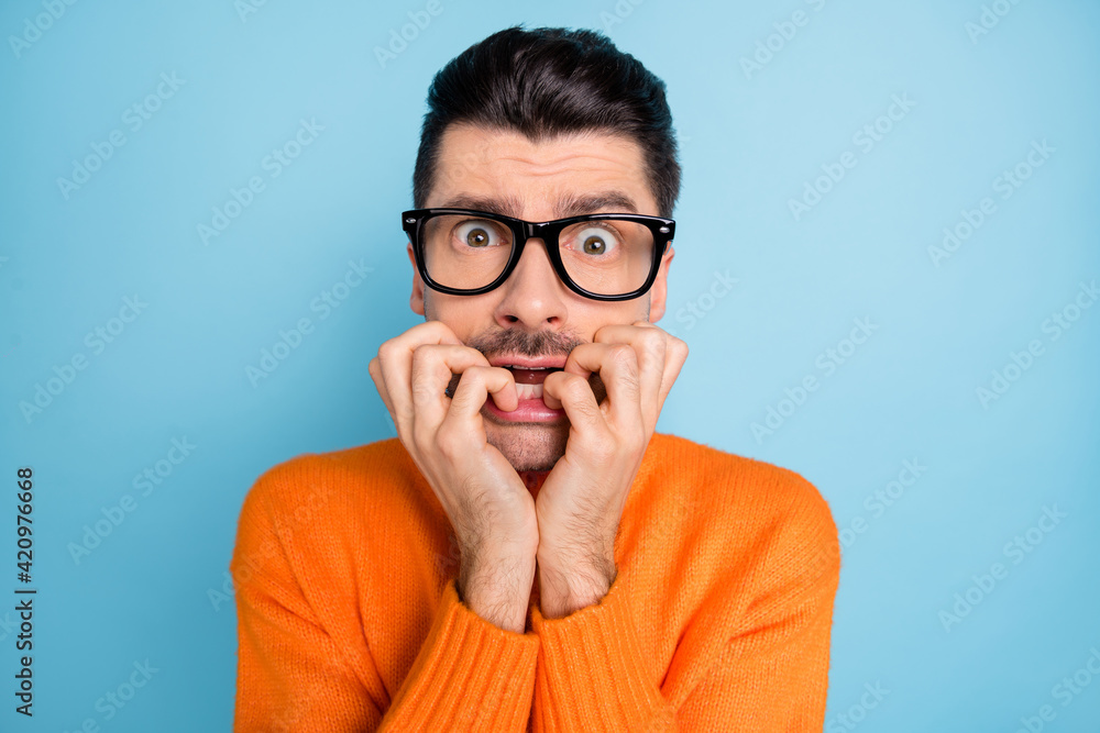 Portrait of nervous handsome guy biting finger nail staring eyewear isolated on blue color background Portrait of nervous handsome guy biting finger nail staring eyewear isolated on blue color background