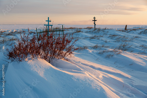 View of the crosses in the snowy tundra on the coast of the frozen sea. An old cemetery in the far North of Russia in the Arctic. Snow-covered graves. Cold winter weather. Chukotka, Siberia, Russia. photo