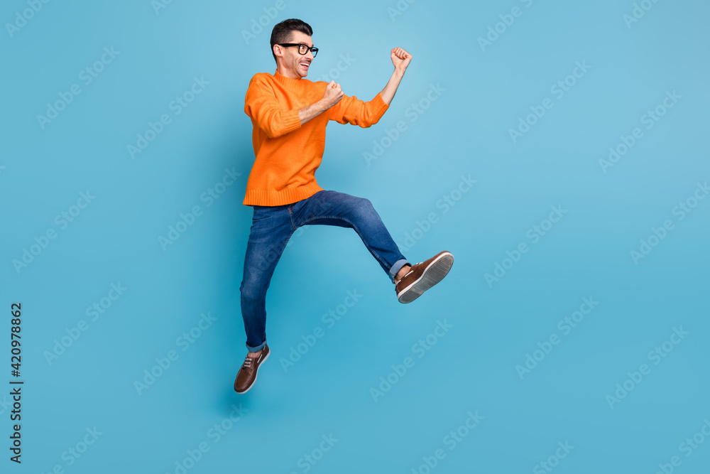 Full length profile portrait of astonished handsome guy fists up jump celebrate isolated on blue color background