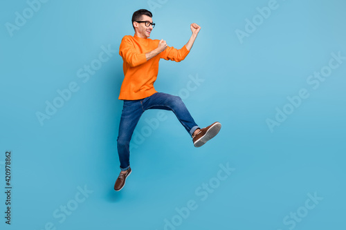 Full length profile portrait of astonished handsome guy fists up jump celebrate isolated on blue color background