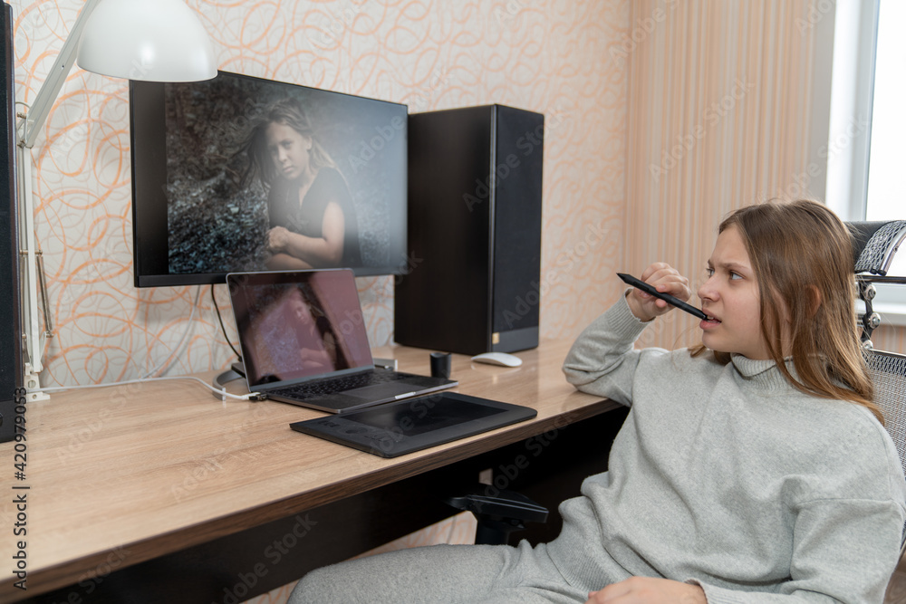 a girl sitting at a computer table, pensively looking at her photo while biting the stylus from a graphics tablet a girl sitting at a computer table, pensively looking at her photo while biting the stylus from a graphics tablet