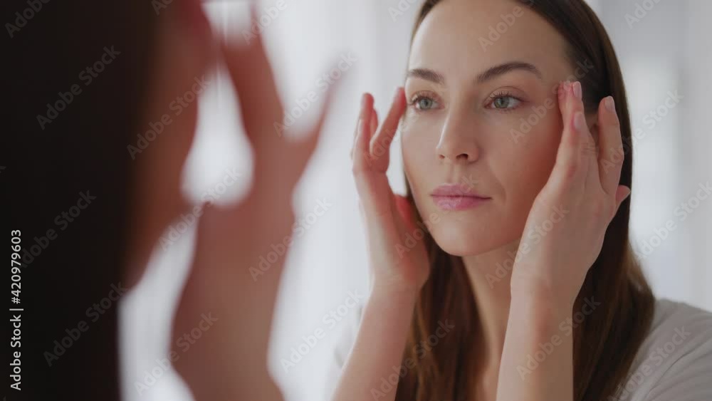 Woman examining perfect skin near mirror