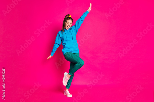 Full length photo of adorable sweet woman dressed blue hoodie dancing rising hand arm isolated vibrant pink color background © deagreez