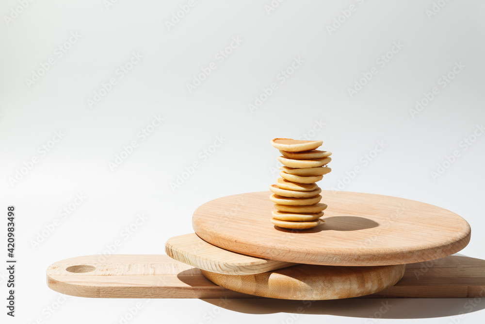 Balancing food. A stack of mini pancakes on a stack of wooden trays. On a light background, a copy of the space, hard shadows Balancing food. A stack of mini pancakes on a stack of wooden trays. On a light background, a copy of the space, hard shadows