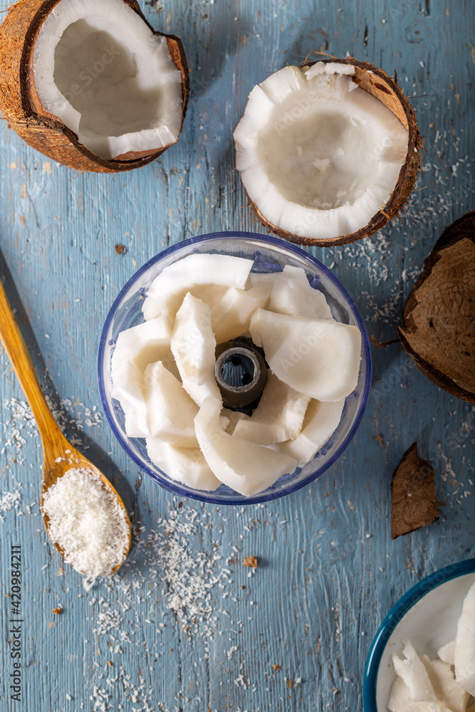 Fototapeta premium Slices of peeled coconut in rondo and coconut flakes in spoon with fresh coconut on wooden table.