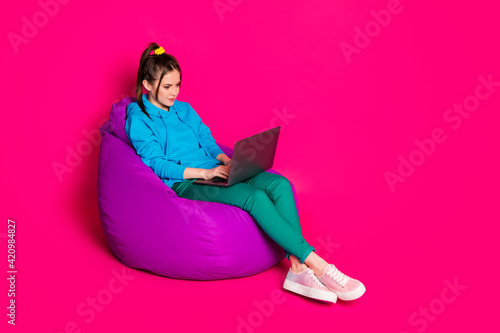 Full length photo of charming young lady wear blue sweater relaxing violet beanbag typing modern device isolated pink color background