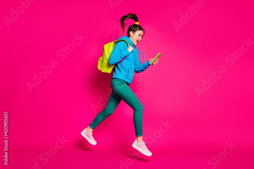 Full length photo of impressed funny young woman dressed blue hoodie rucksack typing modern device isolated pink color background