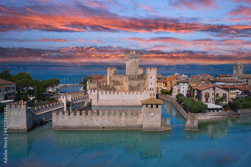 Sirmione, Lake Garda, Italy. The famous Sirmione Castle. Frontal close aerial view. Reflections of the castle in the water in the background pink sky at sunset