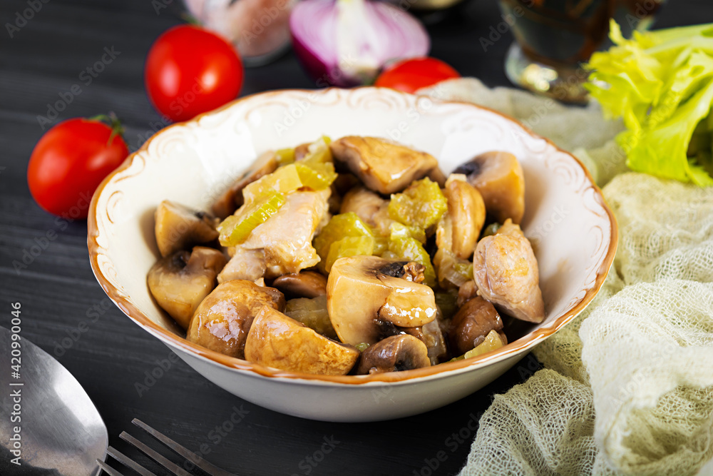 Stew chicken thighs with mushrooms, celery, onion and pepper. Stir fry chicken on wooden background