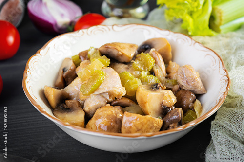 Stew chicken thighs with mushrooms, celery, onion and pepper. Stir fry chicken on wooden background