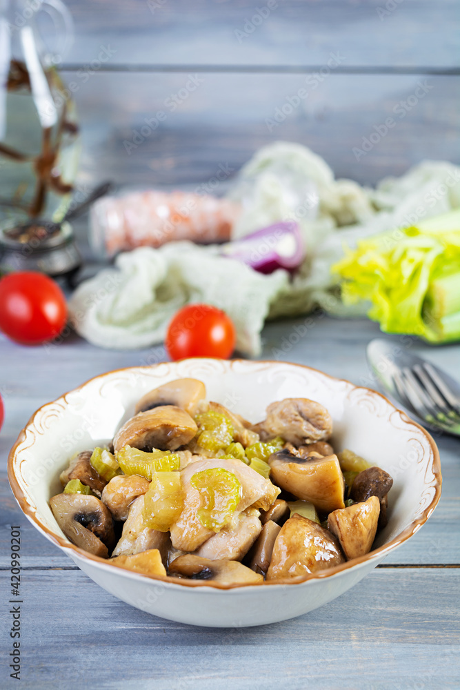 Stew chicken thighs with mushrooms, celery, onion and pepper. Stir fry chicken on wooden background