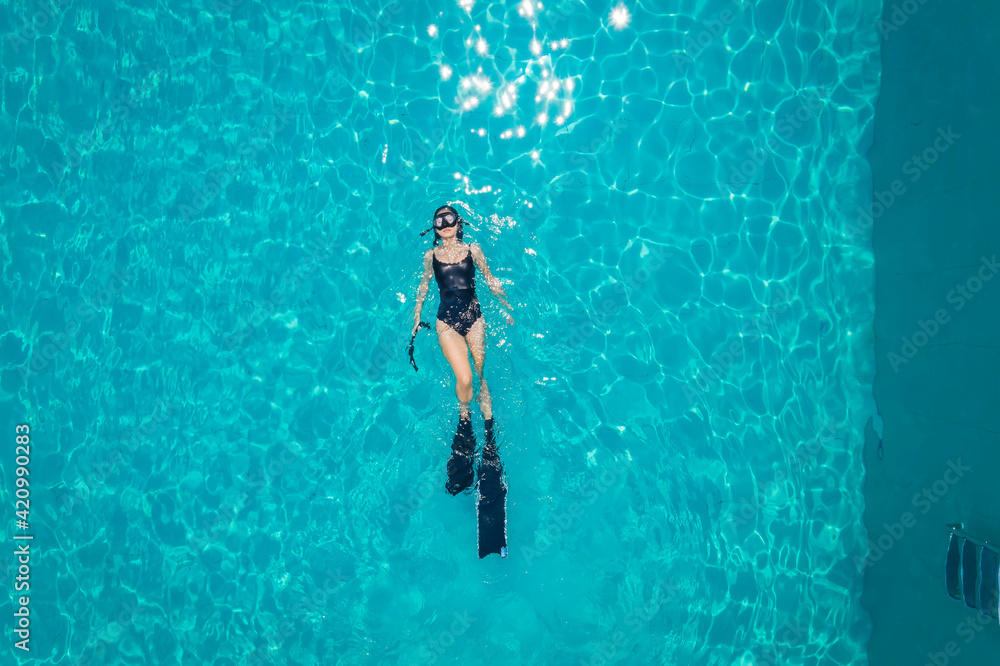 Aerial Top view of female in black swimming suit lying on the poolside,which she is a relax time with snorkeling at a swimming pool