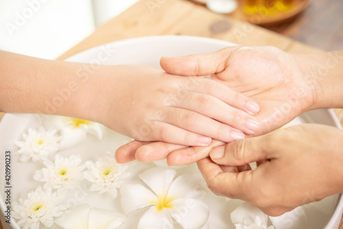 Beautician massaging hand of female spa salon client. Spa treatment and product for female feet and hand spa. white flowers in ceramic bowl with water for aromatherapy at spa.