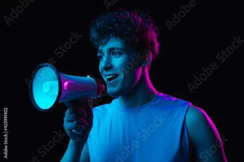 Young man with megaphone isolated on dark multicolored background in neon light