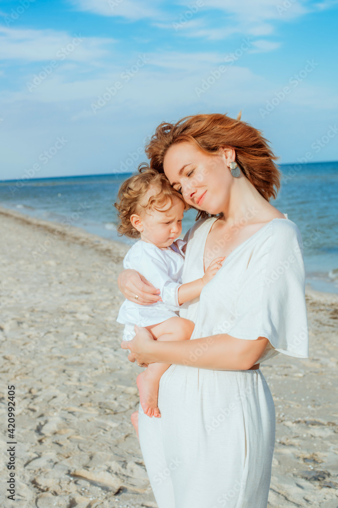 Mom is holding and smiling a little daughter 1 year old with red curly hair in light clothes in the summer on the beach. Happy childhood. Travel and family vacations
Mom is holding and smiling a little daughter 1 year old with red curly hair in light clothes in the summer on the beach. Happy childhood. Travel and family vacations