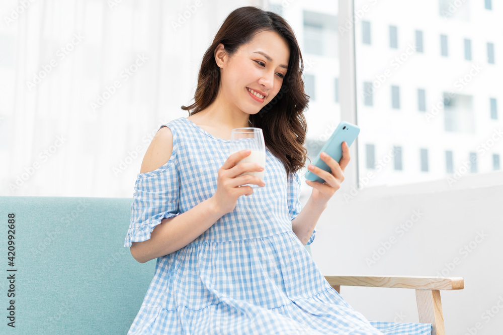 Beautiful pregnant woman holding a cup of milk and listening on the phone