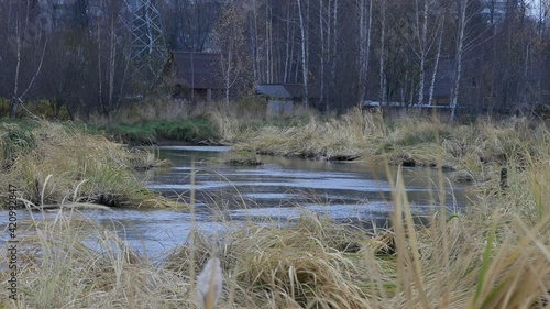 Small house behind a flowing river andwaving grass around it. With woods and city-like background