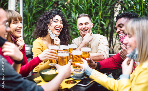 Young people toasting beer wearing open face mask - New normal life style concept with friends having fun together outside at brewery bar garden - Warm filter with focus on woman in yellow clothes