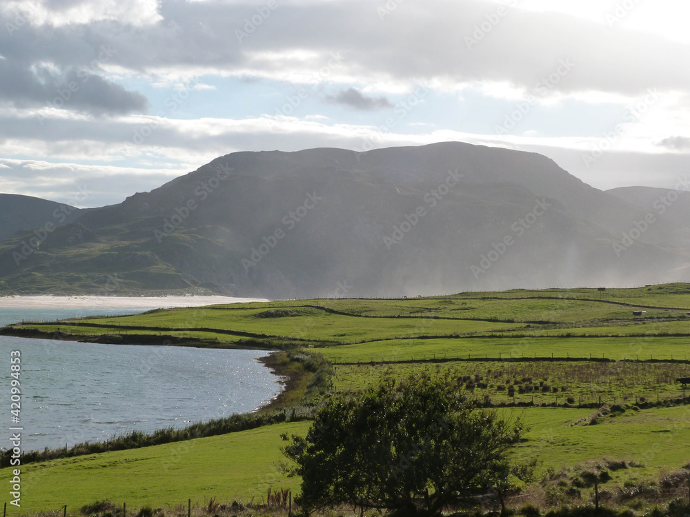 sunny irish landscape with ocean and mountains and green fields