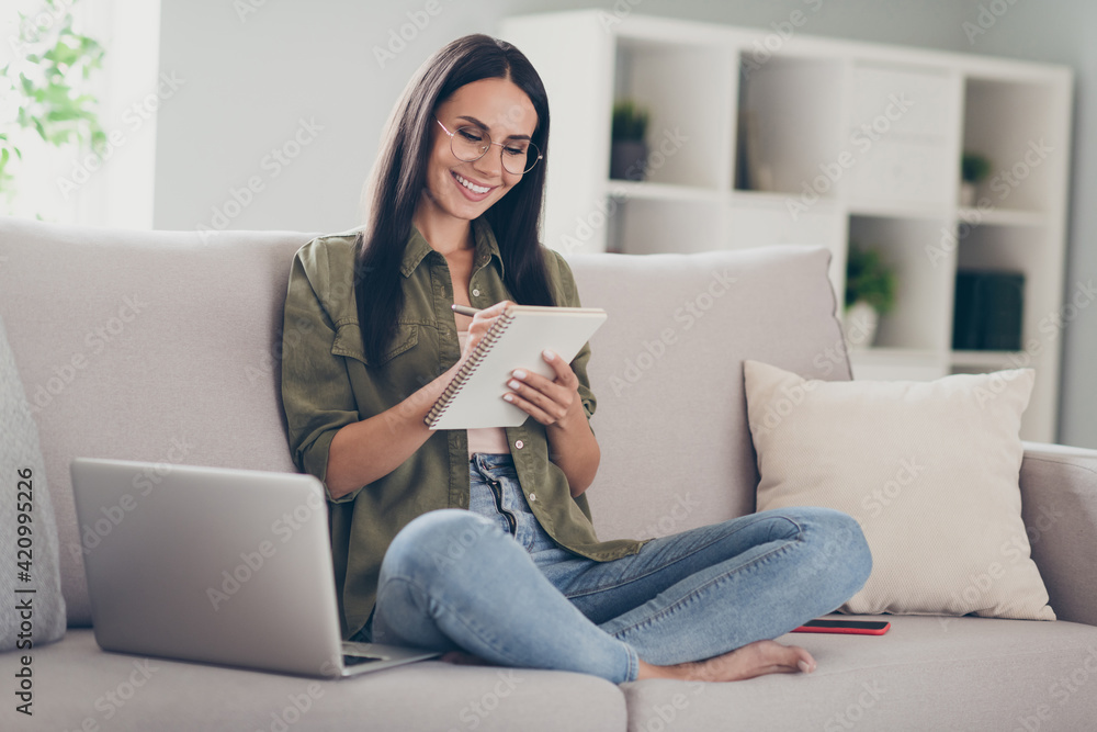 Portrait of lovely cheery girl sitting on divan lotus pose using laptop writing finance plan strategy review at home house flat indoor Portrait of lovely cheery girl sitting on divan lotus pose using laptop writing finance plan strategy review at home house flat indoor