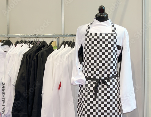 Apron in a chess pattern hung on a doll, in the background a black and white shirt exposed
