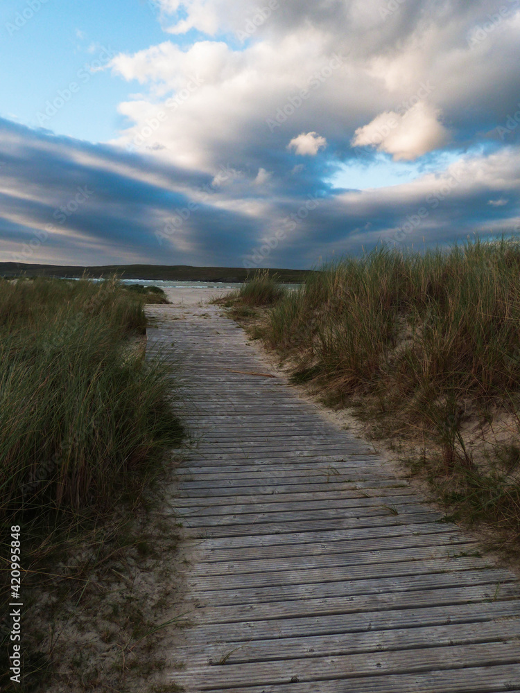 wooden pathway through dunes to the ocean an cloudy sky in ireland