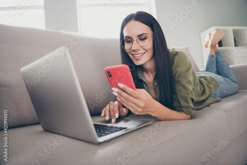 Portrait of lovely focused cheerful girl lying on divan bare foot using laptop device blogging smm at home house flat indoor