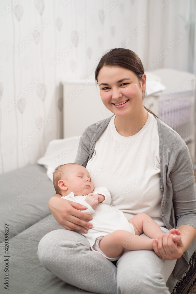 Young mother holding her newborn child. Mom nursing baby. Woman and new born boy relax in a white bedroom. Young mother holding her newborn child. Mom nursing baby. Woman and new born boy relax in a white bedroom.