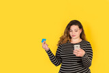 Mujer joven sosteniendo en una mano un télefono móvil y en la otra una una tarjeta de crédito sobre un fondo amarillo liso y aislado. Vista de frente y de cerca. Copy space