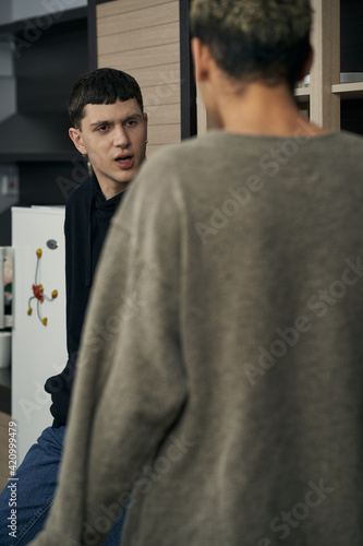 Staged photo illustrates problems and conflicts in gay couple relationships. Moment of showdown: young angry man is standing in front of his partner and talking to him.