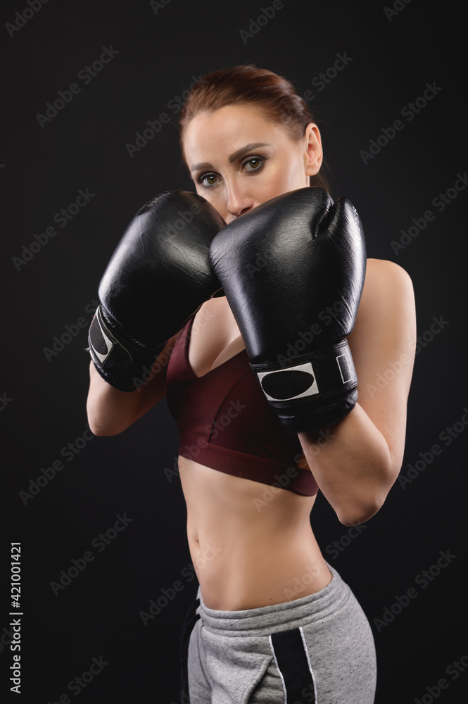 Caucasian fitness girl in boxing gloves stands in a rack on a black background, portrait of a strong and independent woman fighter