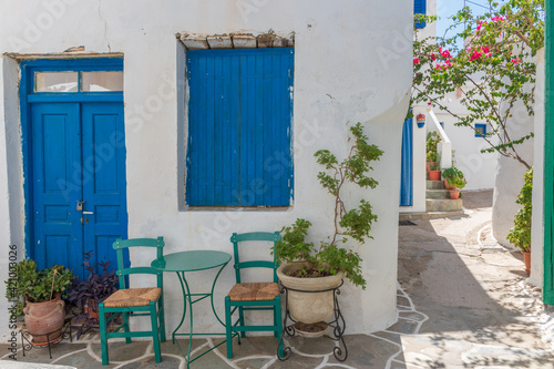 Cycladitic alley with traditional green chairs and table, atypical facade of a house with a blue door and window and a blooming bougainvillea in Chora kythnos, cyclades, Greece.