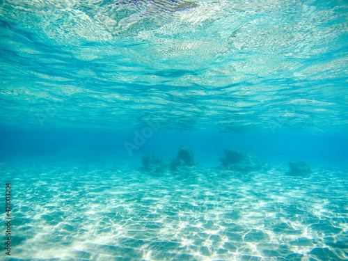 Underwater view on sand sea bottom with group of rocks in distance in sun beam reflections in clear water of Ionian Sea in Greece. Diving azure wild sea water