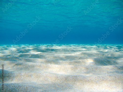 Underwater view on sand sea bottom close-up in sun beam reflections in clear water of Ionian Sea in Greece. Diving azure wild sea water