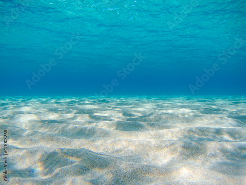 Underwater view on sand sea bottom close-up in sun beam reflections in clear water of Ionian Sea in Greece. Diving azure wild sea water