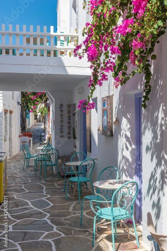 Fototapeta Naklejka Na Ścianę i Meble -  Cycladitic alley with a narrow street and  an exterior  of a traditional  whitewashed cafe with chairs and tables  in Chora kythnos,cyclades, Greece.