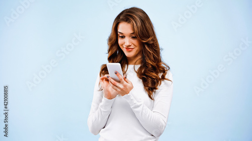 happy woman chatting on smartphone isolated on blue