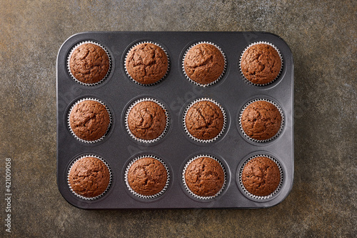 Homemade chocolate cupcakes in baking form on wooden background, top view