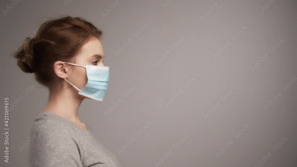 Profile portrait of young woman putting on protective medical mask, studio background. Woman putting on medical face protective mask, virus prevention. Real time. Social distancing and new normal. Profile portrait of young woman putting on protective medical mask, studio background. Woman putting on medical face protective mask, virus prevention. Real time. Social distancing and new normal.