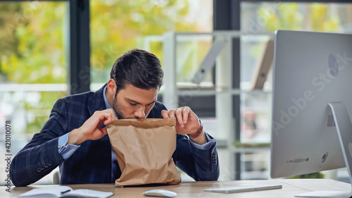 businessman smelling paper bag with takeaway food in office