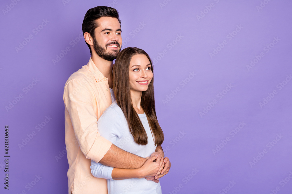 Photo of happy young married couple stand look dream empty space hug isolated on purple color background Photo of happy young married couple stand look dream empty space hug isolated on purple color background