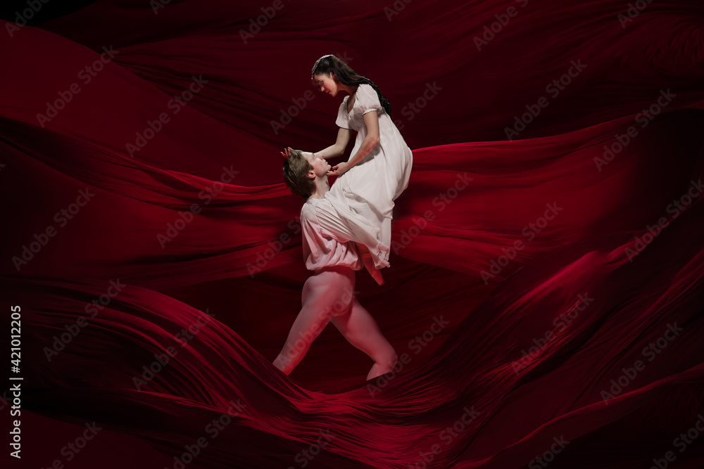 Wine. Young and graceful ballet dancers on red cloth background in classic action. Art, motion, action, flexibility, inspiration concept. Flexible caucasian couple with billowing red waves. Wine. Young and graceful ballet dancers on red cloth background in classic action. Art, motion, action, flexibility, inspiration concept. Flexible caucasian couple with billowing red waves.