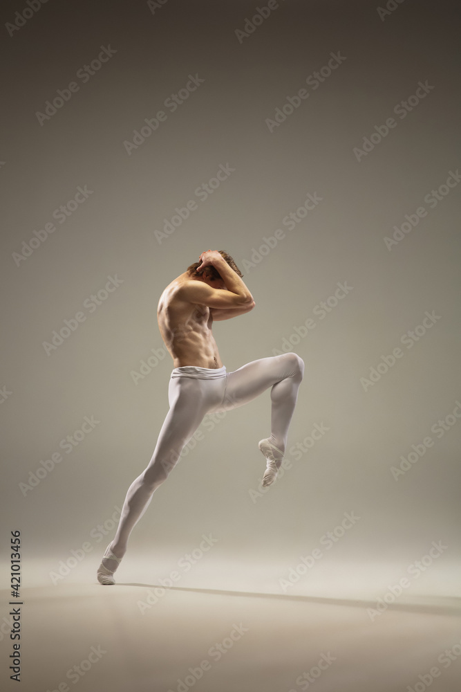 Courageasly. Young and graceful ballet dancer isolated on studio background in flight, jump. Art, motion, action, flexibility, inspiration concept. Flexible caucasian ballet dancer, moves in glow.