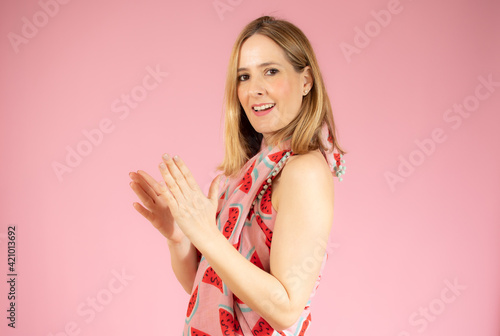 Young woman feeling happy and successful, smiling and clapping hands isolated over pink background.