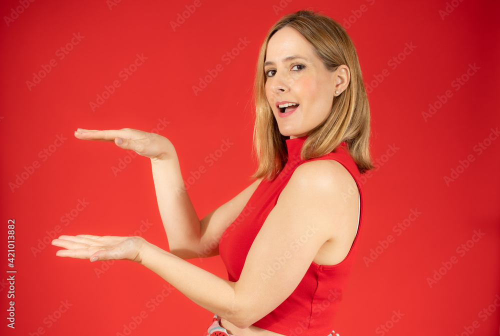 Young caucasian woman posing isolated over red background holding something with both hands, product presentation. Young caucasian woman posing isolated over red background holding something with both hands, product presentation.