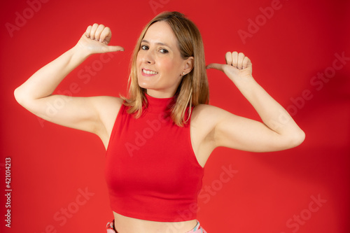Smiling young woman in casual dress posing isolated over red background. People sincere emotions lifestyle concept. Mock up copy space. Pointing thumbs on herself.